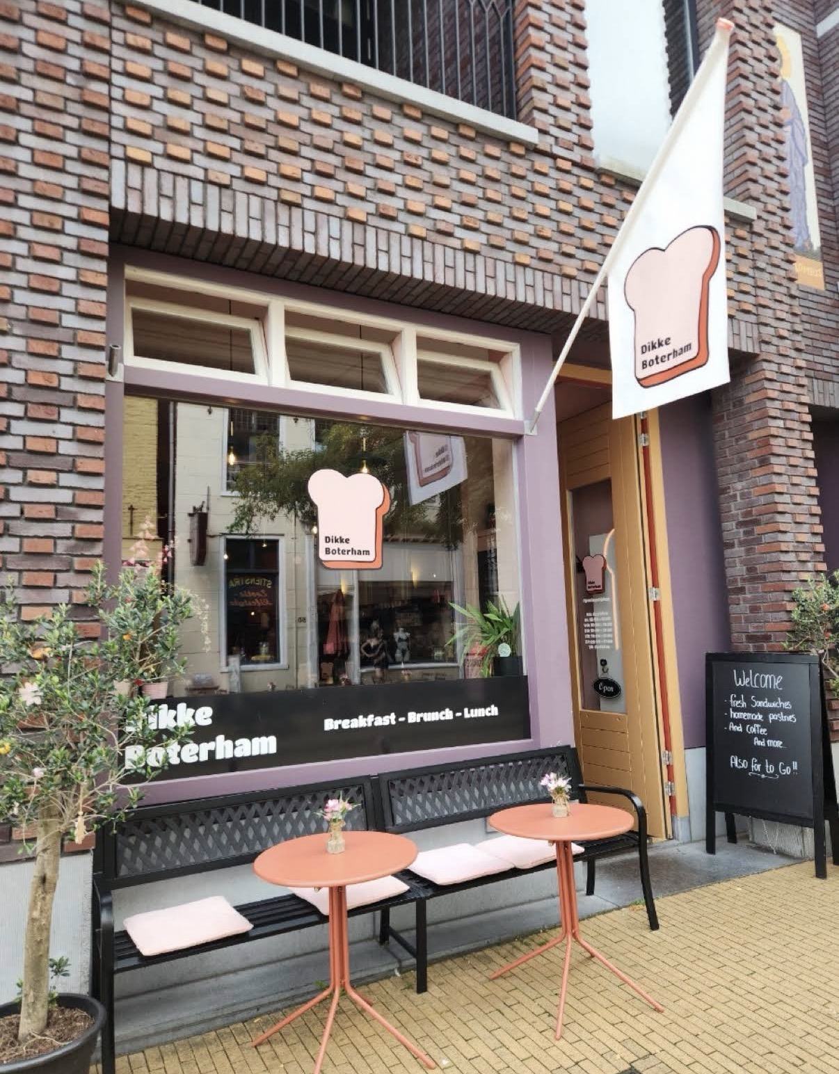 De gevel van Dikke Boterham aan de Steentilstraat met roze logo-vlag en terras